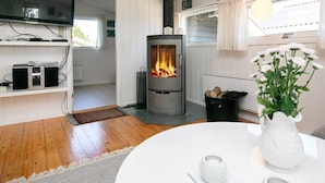 A cozy room with a wood-burning stove, a television on a shelf, and a white table with a vase and candle.