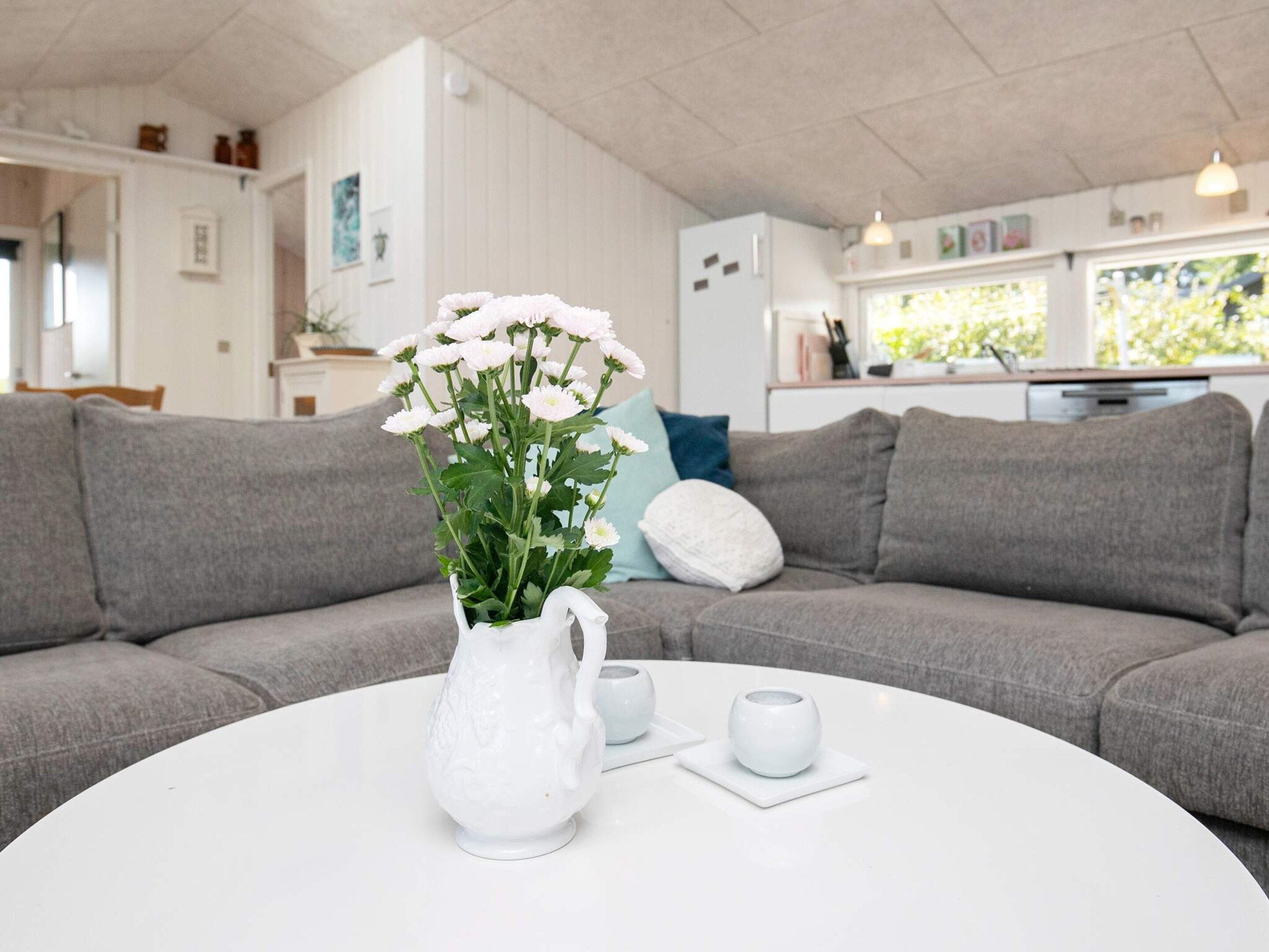 Una sala de estar con un sofá gris, una mesa de centro blanca y un jarrón blanco con flores.