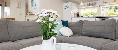 Una sala de estar con un sofá gris, una mesa de centro blanca y un jarrón blanco con flores.