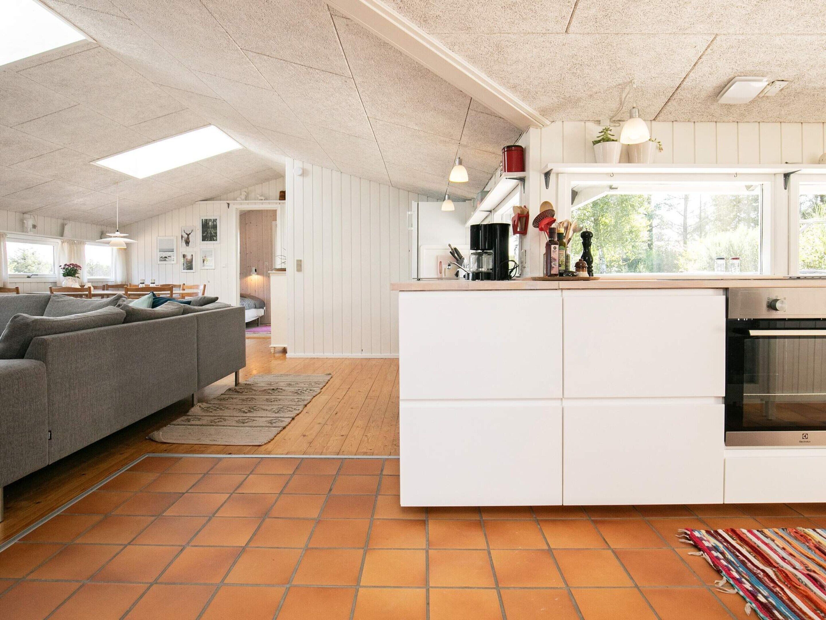 A modern kitchen with white cabinetry, a built-in oven, and a dining area with a grey sofa and wooden dining table.