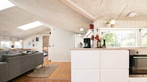 A modern kitchen with white cabinetry, a built-in oven, and a dining area with a grey sofa and wooden dining table.