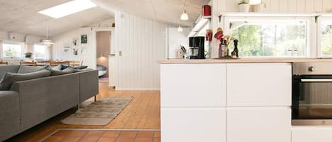 Eine moderne Küche mit weißen Schränken, einem eingebauten Ofen und einem Essbereich mit grauem Sofa und Holztisch.