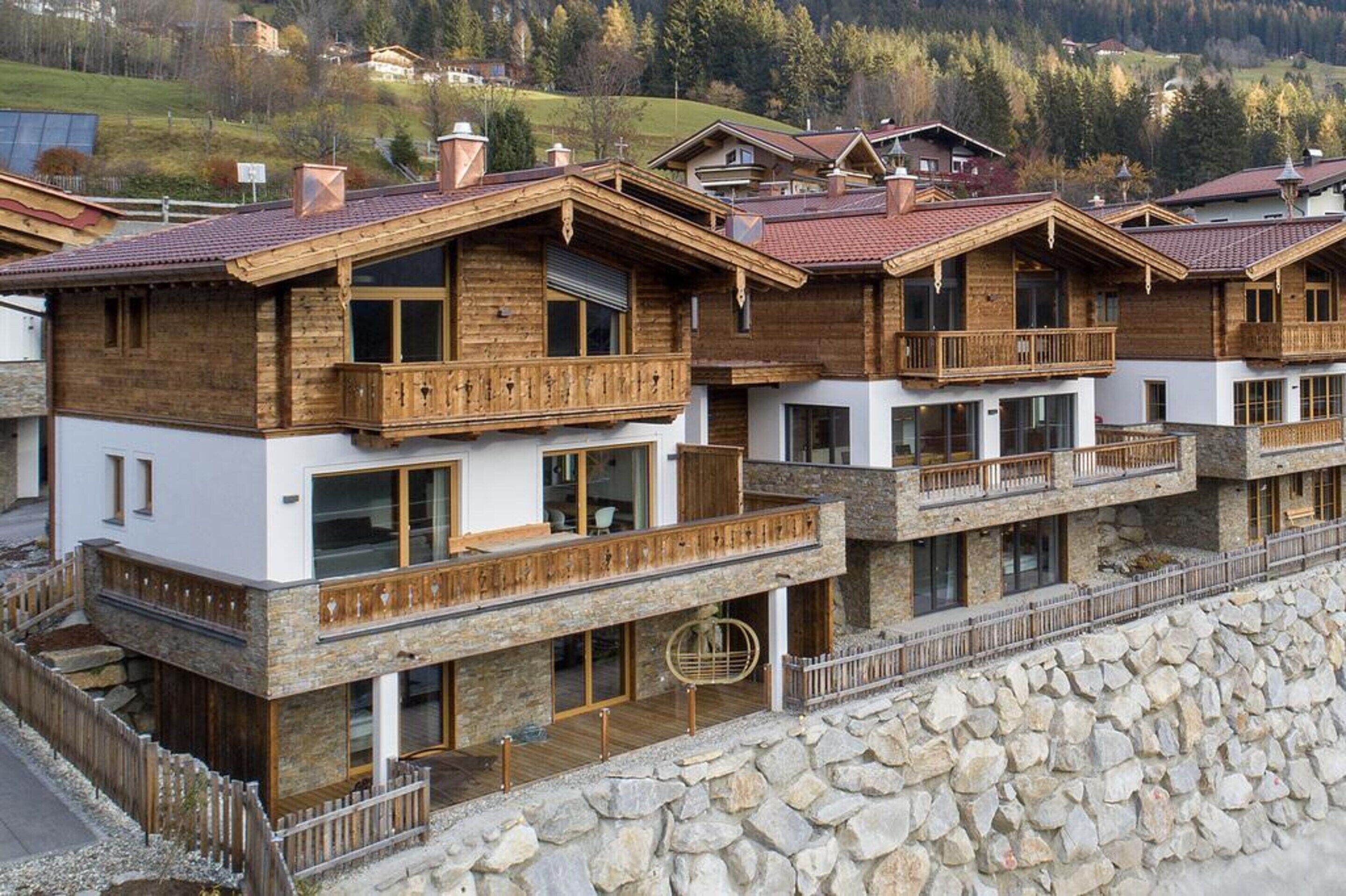 Una hilera de edificios tipo chalet de madera con balcones, cimientos de piedra y un paisaje montañoso al fondo.