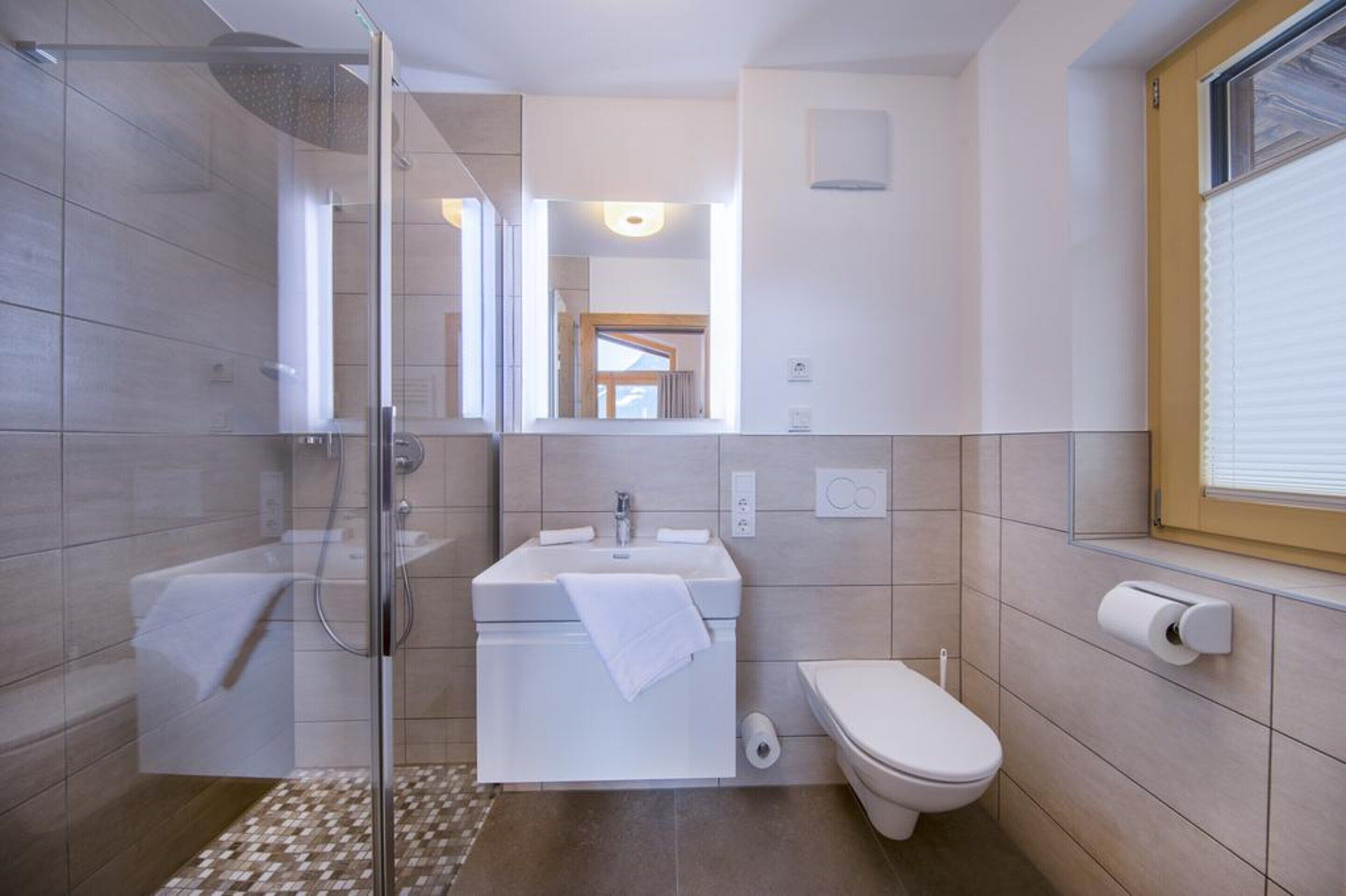 Une salle de bain moderne avec une douche en verre, un lavabo avec une serviette, des toilettes et une fenêtre avec des stores.