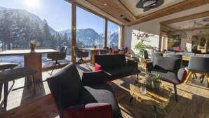Ein modernes Interieur mit Holzbalkendecke, großen Fenstern mit Bergblick und einer gemütlichen Sitzecke mit Tisch und Stühlen.