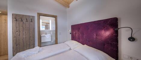 A bedroom with a wooden ceiling, a bed with white linens, a purple headboard, and a mirror on the wall.