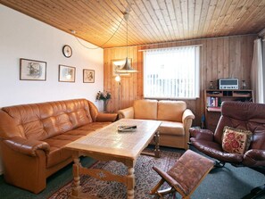 Uma sala de estar acolhedora com teto de madeira, sofás de couro, mesa de centro de madeira, uma televisão pequena e uma estante de livros.