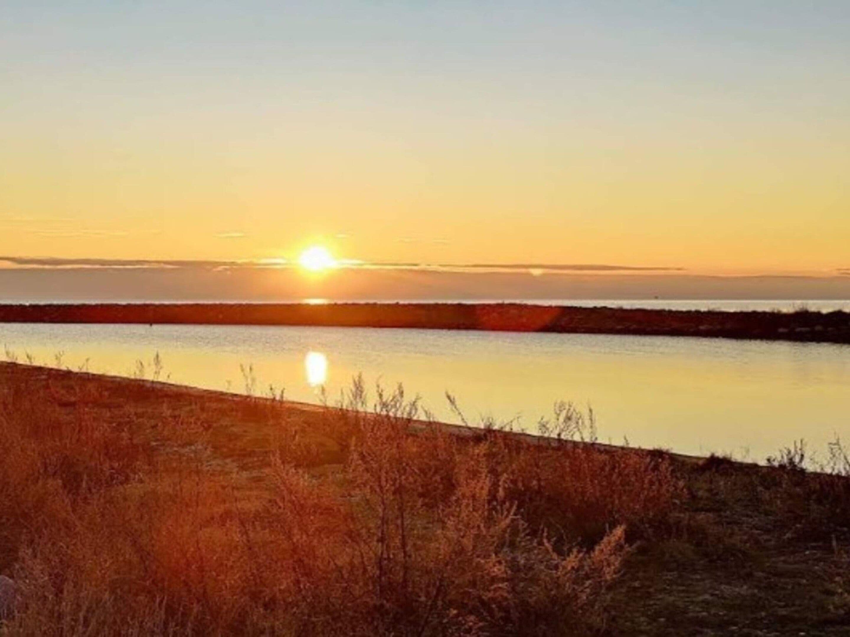 A sunset over a calm body of water with a grassy foreground.