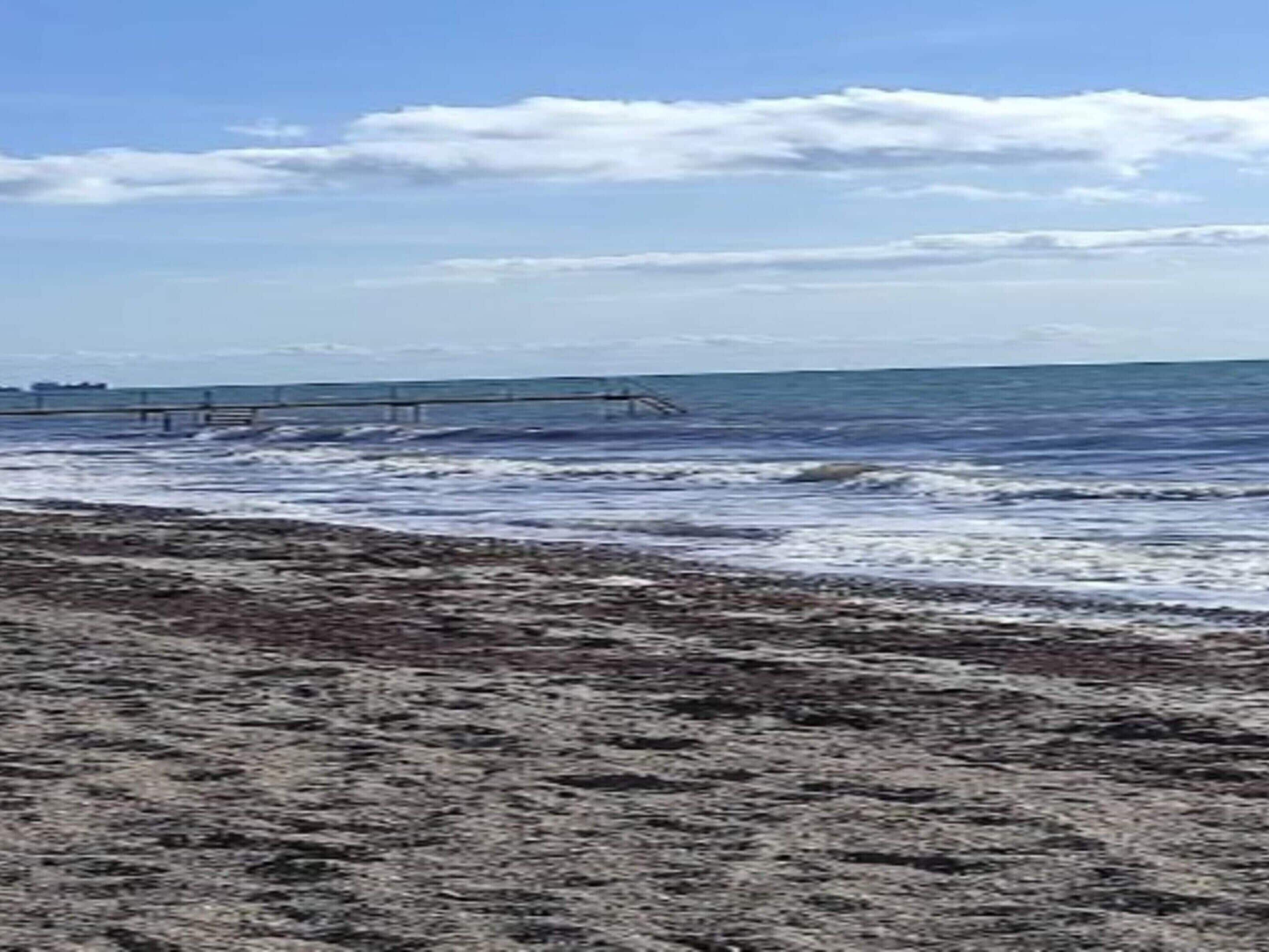 Una playa con olas y un muelle al fondo.