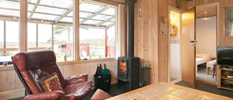 A cozy room with a wooden ceiling, a large window, a leather chair, a table with a remote control, and a television.