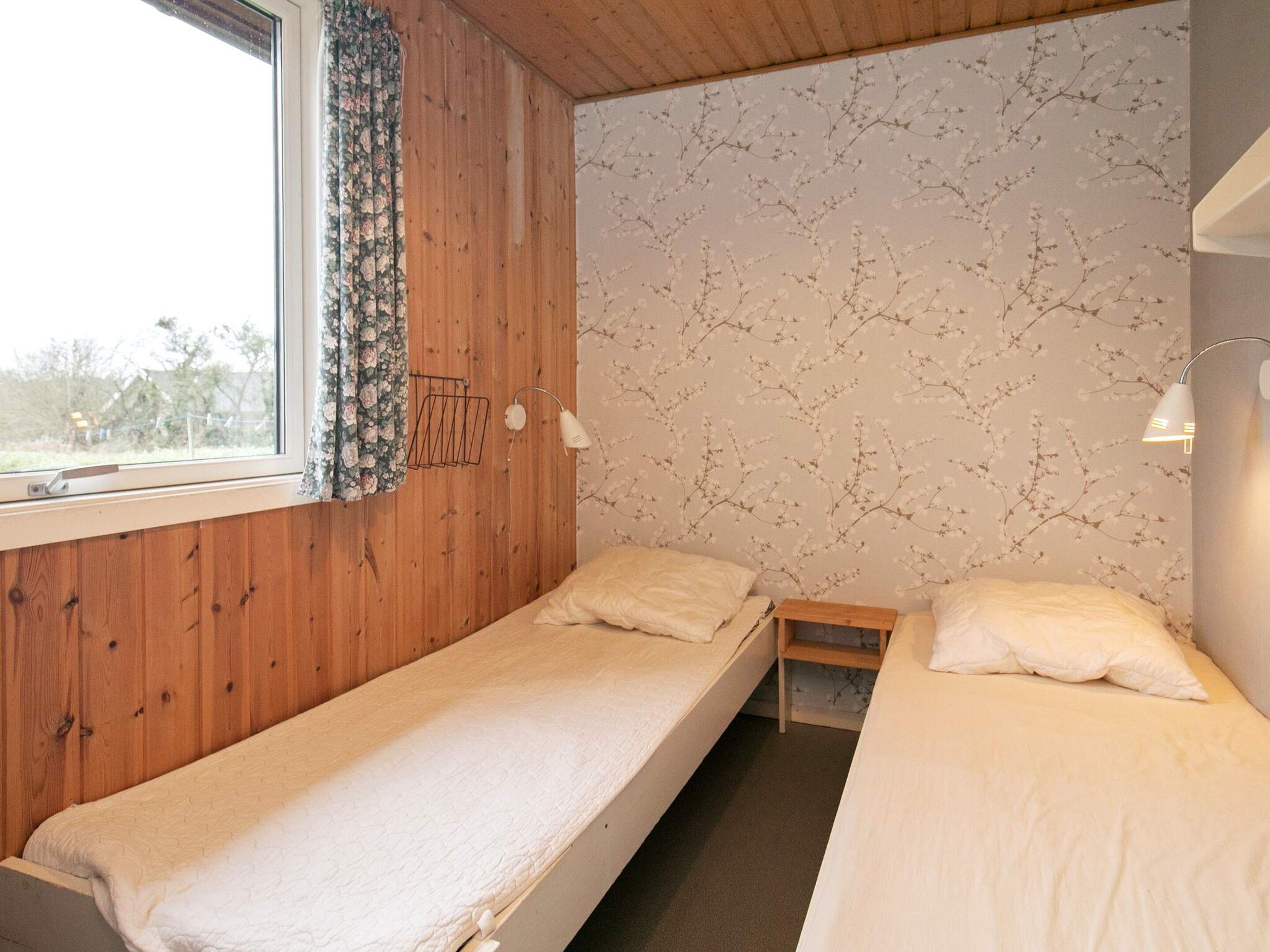 A room with two single beds, a window with curtains, a wall-mounted lamp, and a patterned wallpaper.