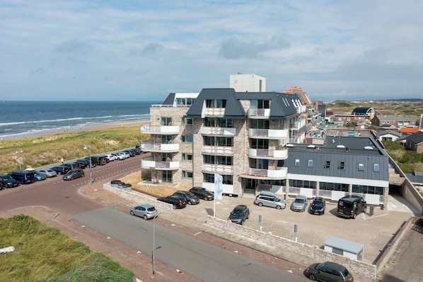 A multi-story hotel with balconies, a parking lot, and a view of the beach and ocean. - Apartment in Egmond aan Zee Near the Beach (Egmond aan Zee)