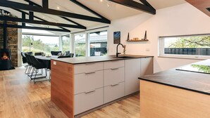 A modern kitchen with a large island, wooden beams, and a dining area with a view. - Holiday Home in Saltum (Saltum)