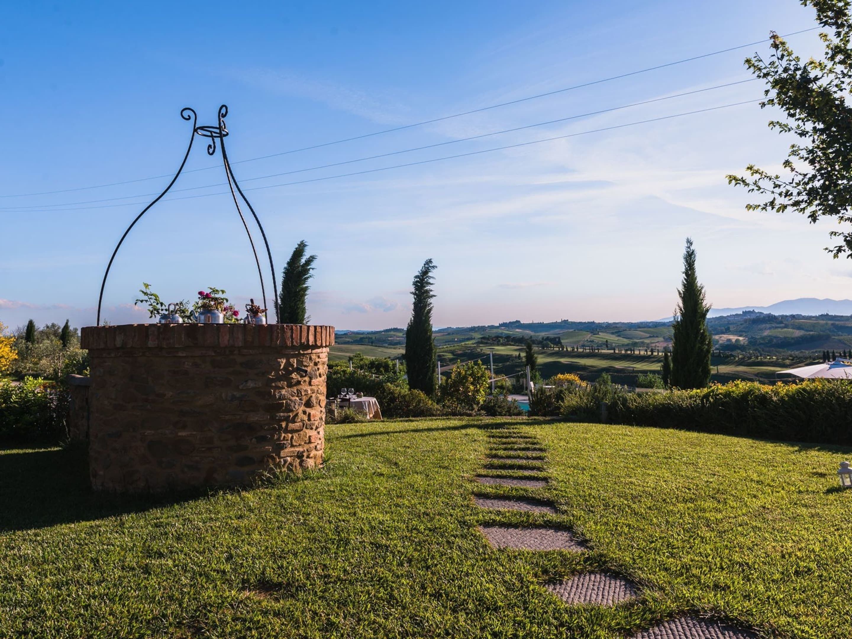 A stone structure with a metal archway, a grassy path leading to a scenic view of hills and trees.