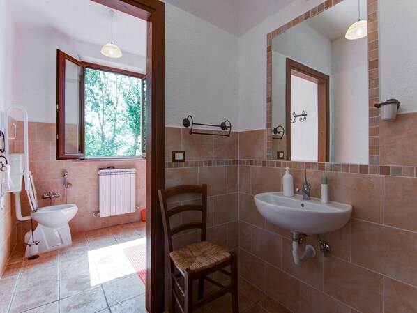 A bathroom with a toilet, bidet, sink, and chair.