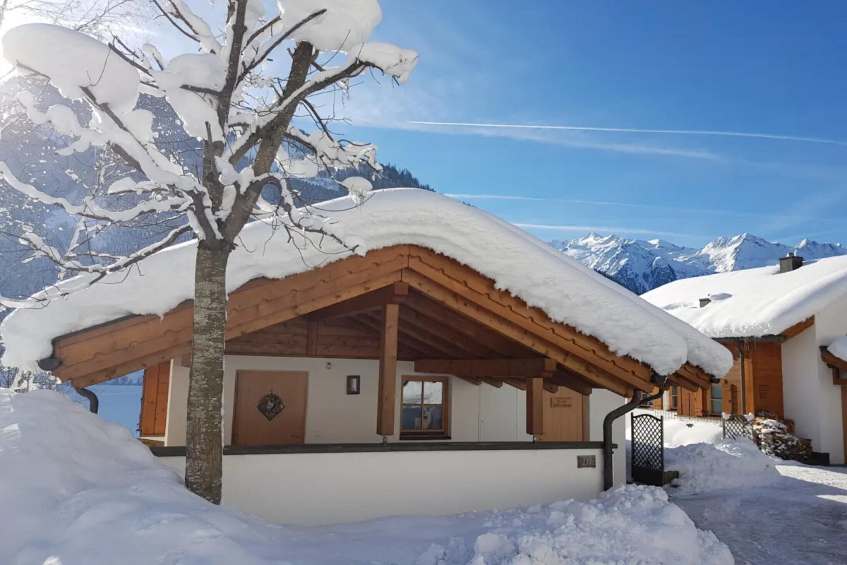 Un chalet en bois, dont le toit est recouvert de neige, entouré de neige et de montagnes.