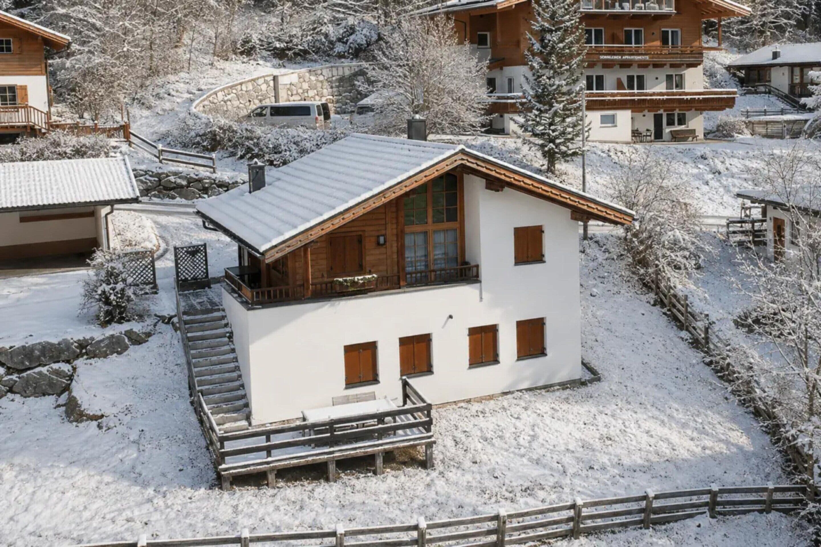 A two-story chalet with a balcony, wooden exterior, and a stone staircase leading to the entrance.