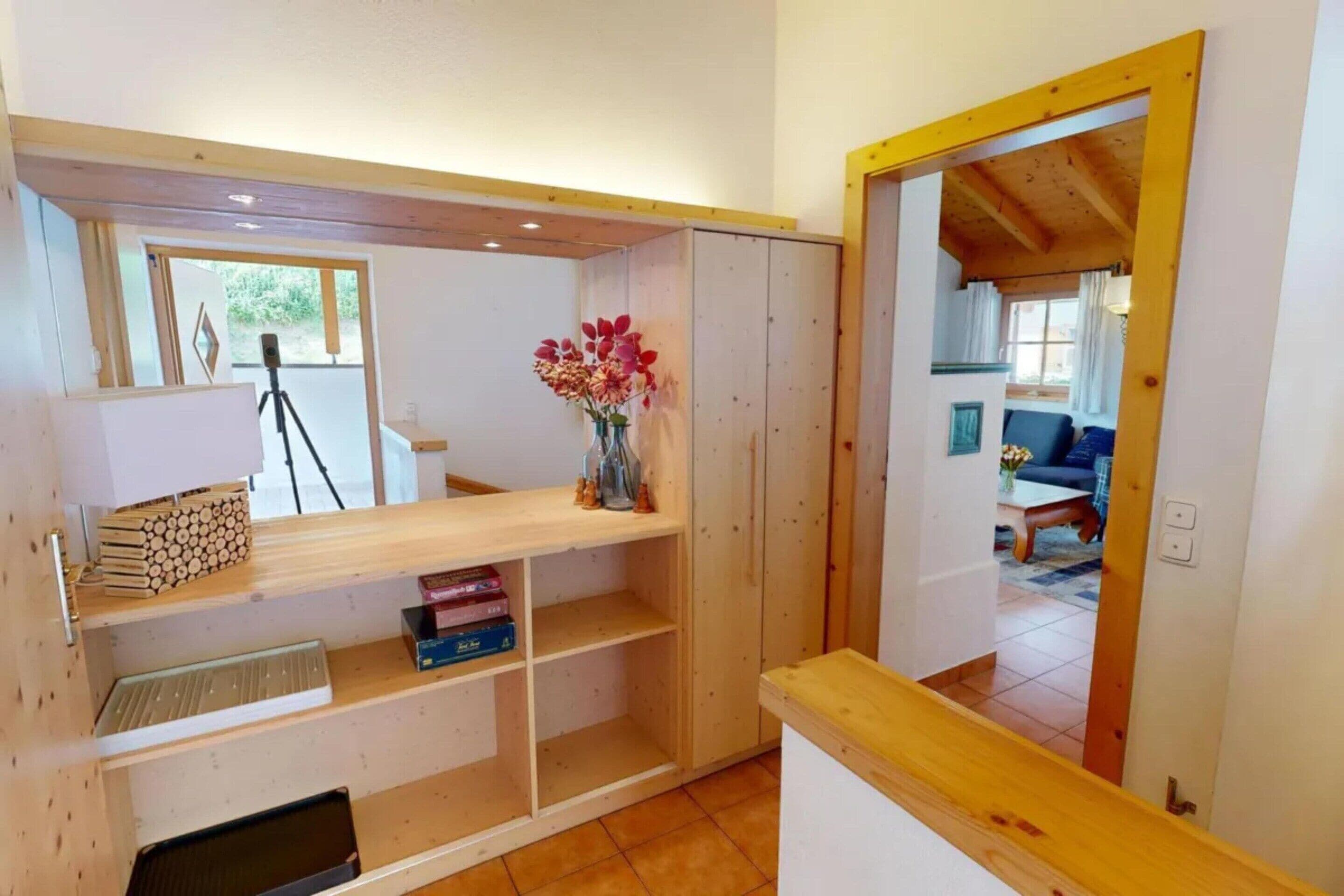 A room with a wooden desk, shelves, a tripod, and a vase with flowers.