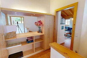 Une pièce avec un bureau en bois, des étagères, un trépied et un vase rempli de fleurs.