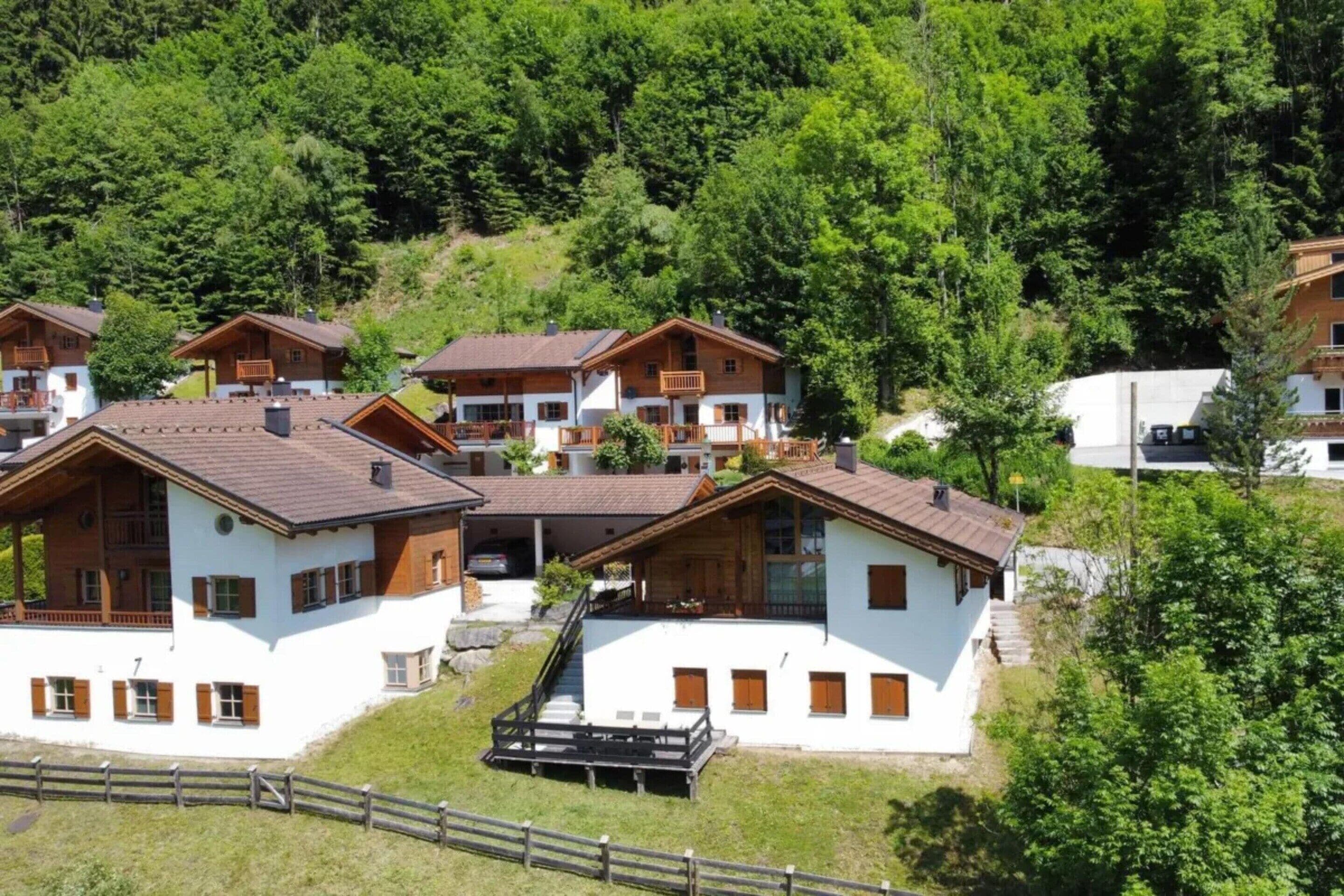 A cluster of chalet-style buildings with sloped roofs, wooden balconies, and a white facade, surrounded by dense forest.