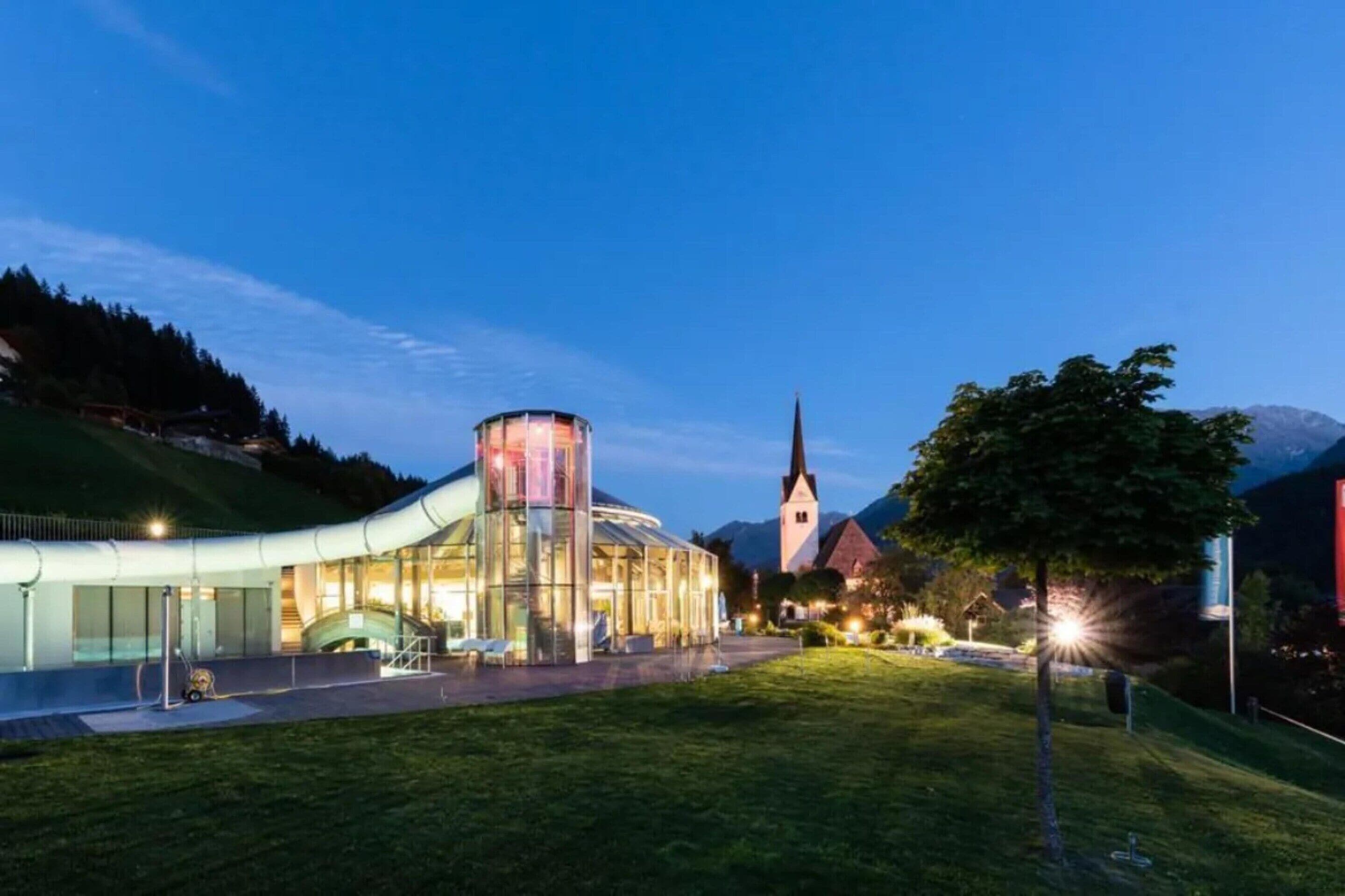 A modern building with a glass facade, a church with a tall spire, and a grassy area in the foreground.