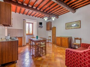 A cozy kitchen with wooden cabinets, a dining table with chairs, a red sofa, and a tiled floor.