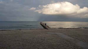 A beach with a wooden pier extending into the sea, under a cloudy sky.
