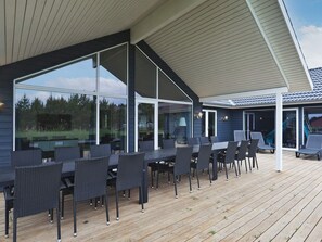 A covered outdoor patio with a dining area, large windows, and a view of the surrounding landscape.