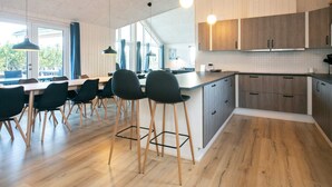A modern kitchen with wooden cabinets, a dining area with chairs, and a large window providing natural light.