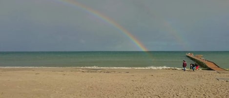 Une plage avec un arc-en-ciel, une jetée et quelques personnes.