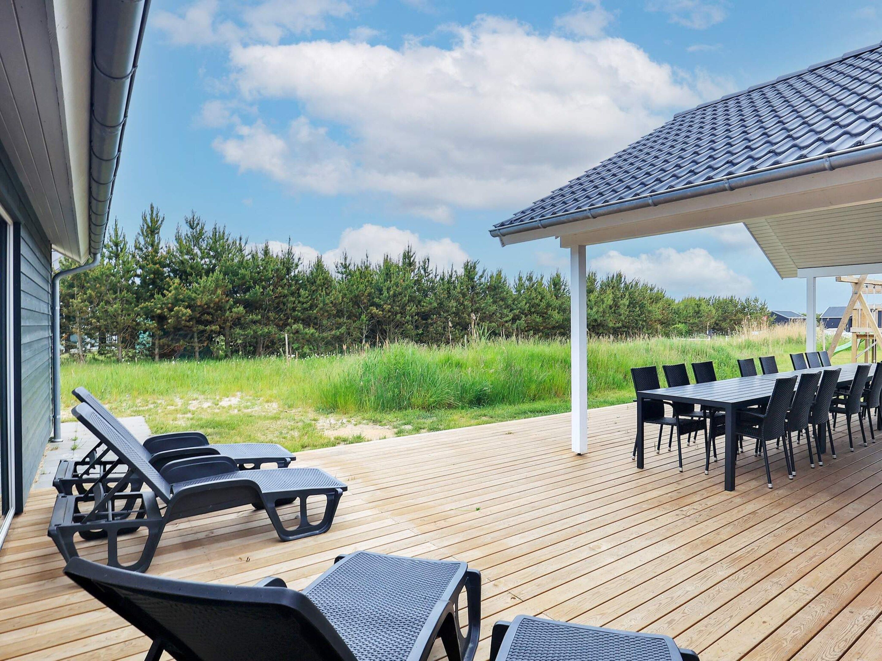 Une terrasse en bois avec des chaises longues et une table, donnant sur une pelouse et des arbres.