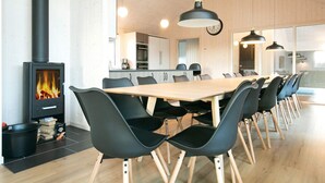 A modern kitchen with a wood-burning stove, a dining area with a long table and chairs, and pendant lighting.