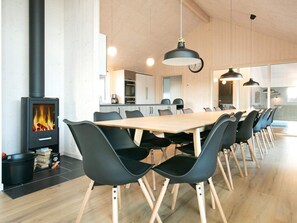 Una cocina moderna con estufa de leña, comedor con mesa larga y sillas, e iluminación colgante.