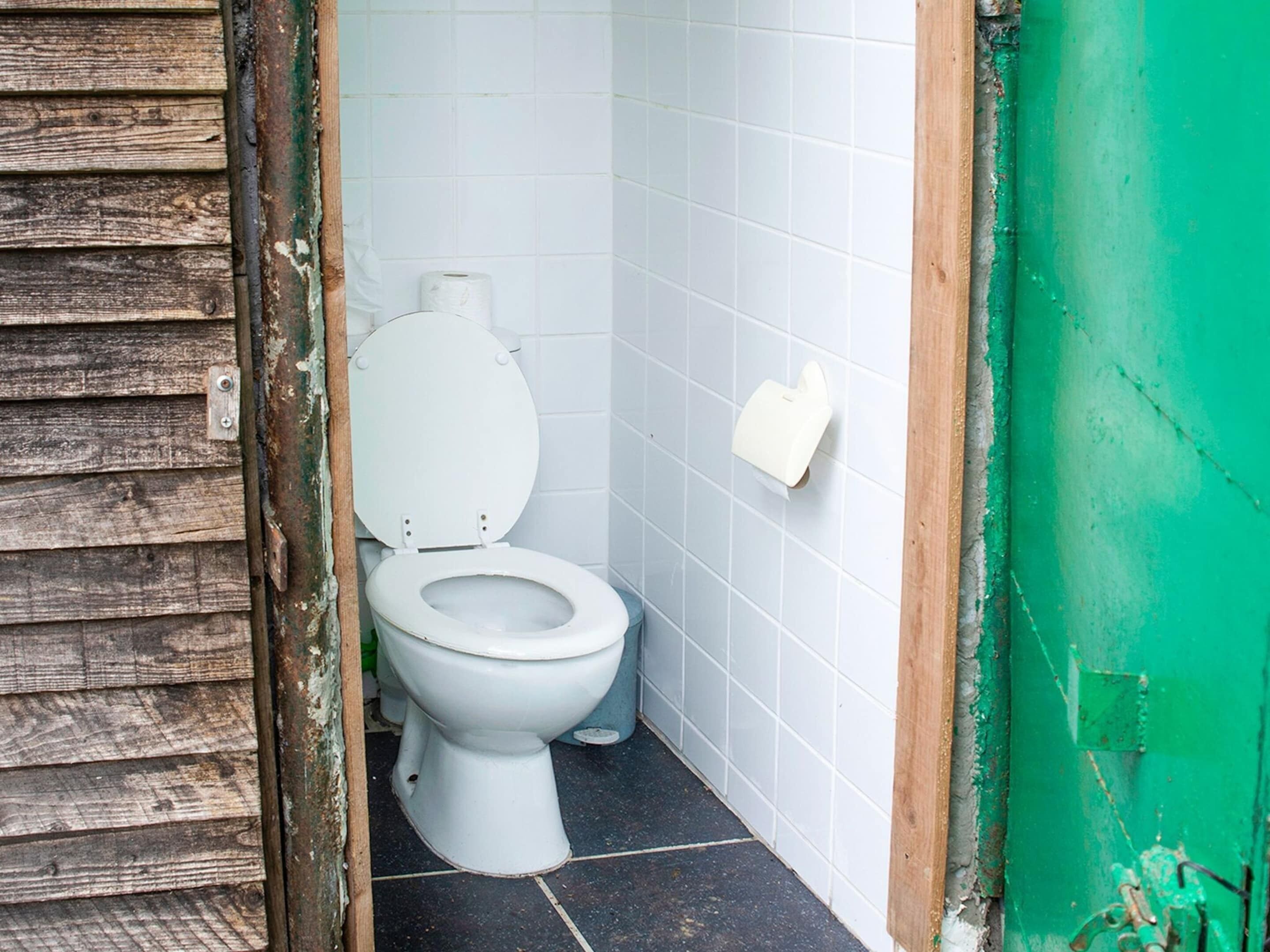 A small, compact bathroom with a white toilet, a toilet paper holder, and a wooden door frame.