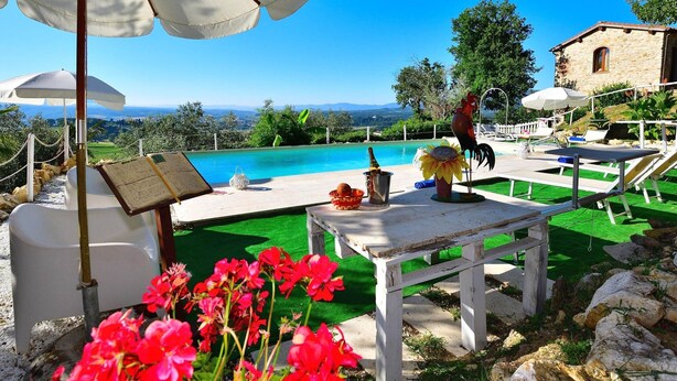 A poolside area with a view of the landscape, outdoor seating, and a rooster statue. - Rustic Elegance Near Florence (Rignano sull'Arno)