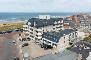 A multi-story hotel with balconies, a parking lot, and a view of the beach and ocean. - Apartment in Egmond Near the Beach (Egmond aan Zee)