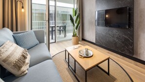 Ein modernes Wohnzimmer mit einer Couch, einem Couchtisch, einem an einer Marmorwand montierten Fernseher und einem Balkon mit Tisch und Stühlen.