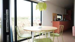 A modern dining area with a round table and four green chairs, large windows, and a view of the outdoors. - Lodge in Callantsoog Near North Sea Beach (Callantsoog)