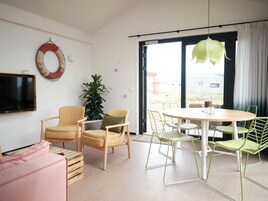 A modern living room with a wooden TV stand, two yellow armchairs, a green plant, and a dining table with green chairs.