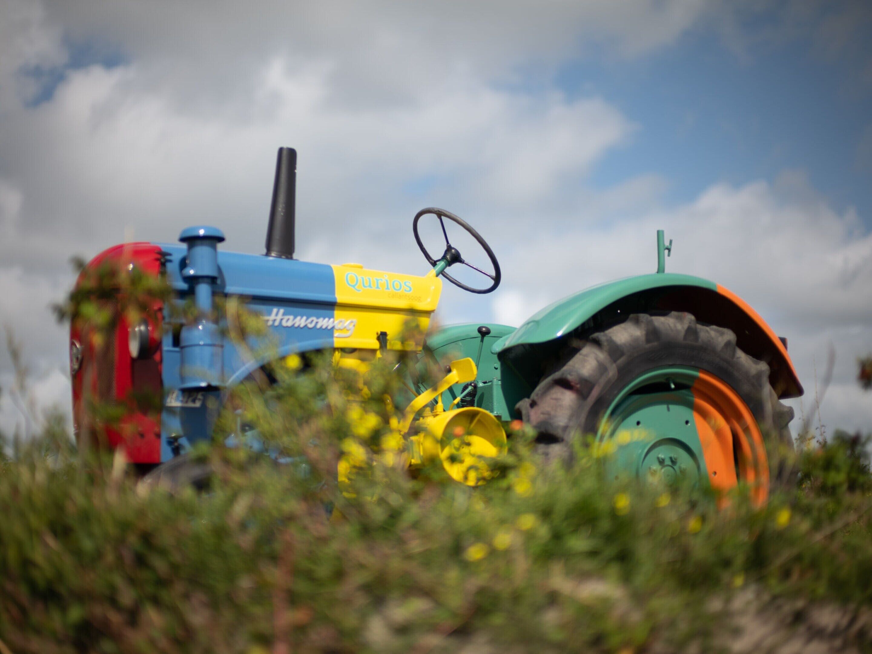 Ein Traktor mit Lenkrad und Fahrerkabine, umgeben von viel Grün und einem bewölkten Himmel.