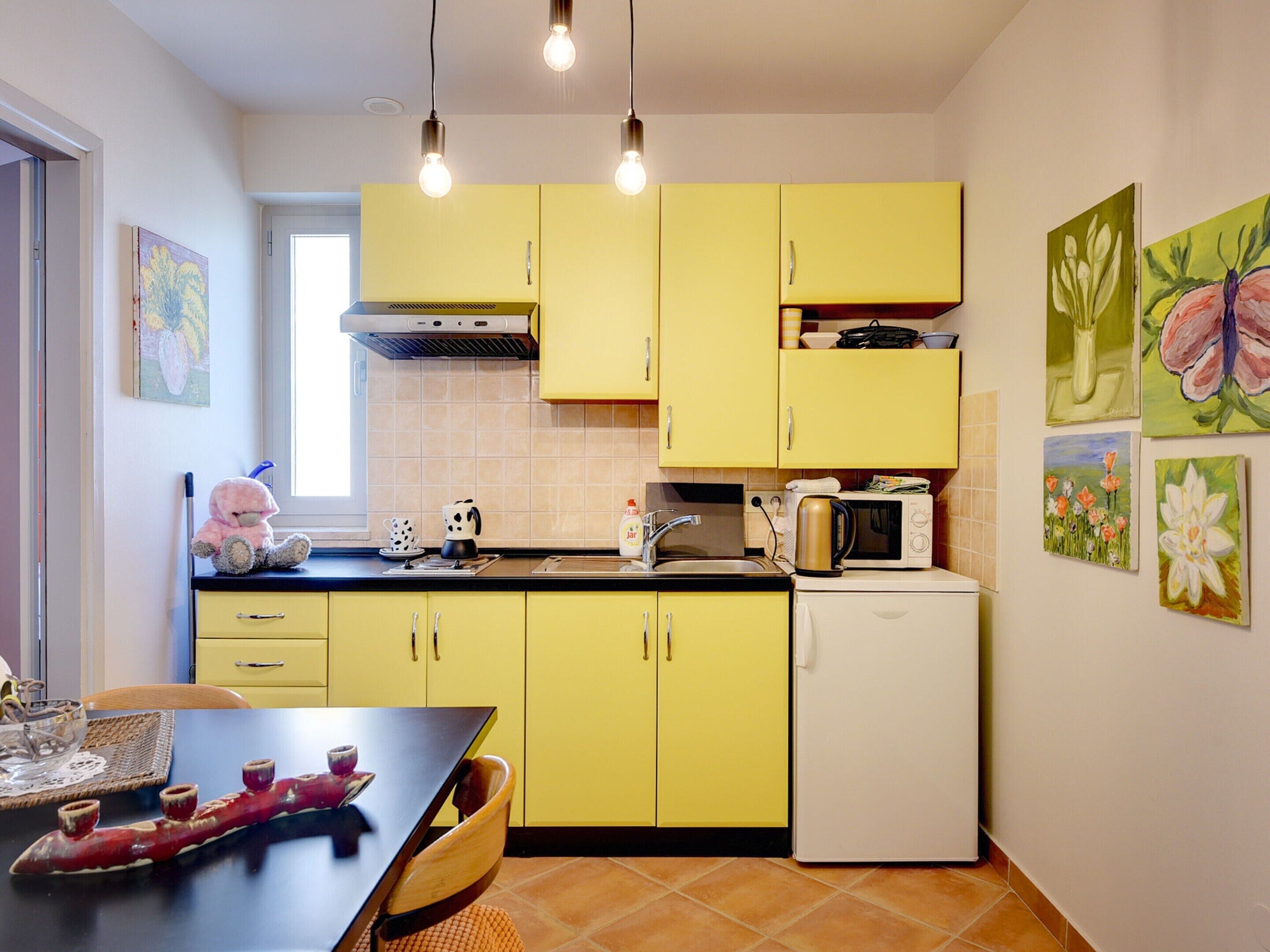 Eine kleine Küche mit gelben Schränken, einem weißen Kühlschrank und einem Essbereich mit Tisch und Stühlen.
