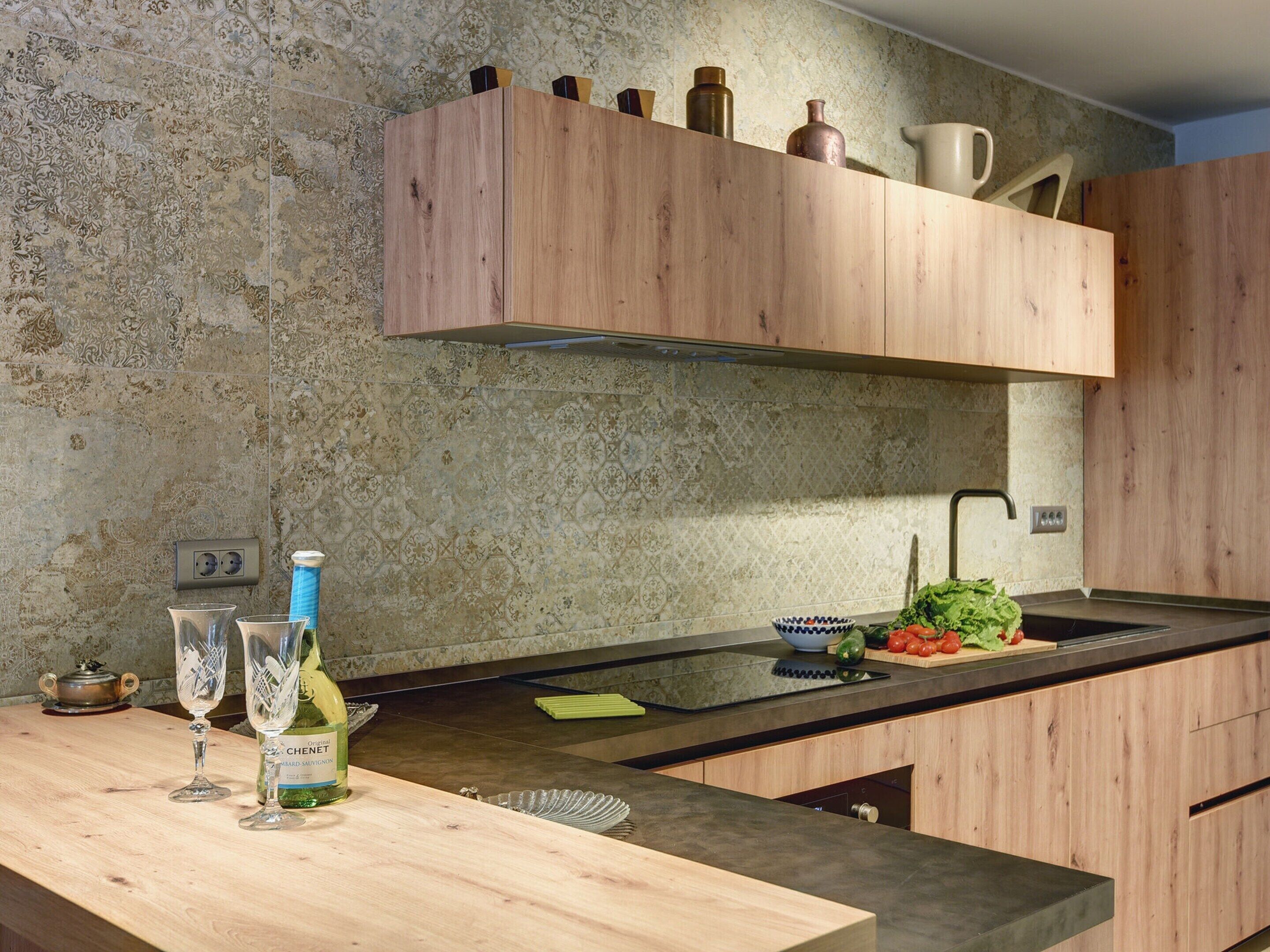 A modern kitchen with wooden cabinets, a black countertop, and a backsplash with a textured pattern.