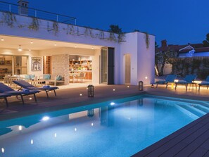 Un espace piscine extérieur moderne, doté de chaises longues et d’un coin repas.