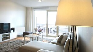 Une chambre d’hôtel moderne dotée d’un grand lit, d’une télévision à écran plat, d’une petite table et d’un balcon avec des chaises.
