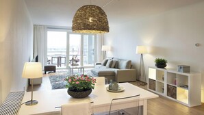 Un salon moderne comprenant une table à manger, un canapé, un meuble blanc et une grande fenêtre.