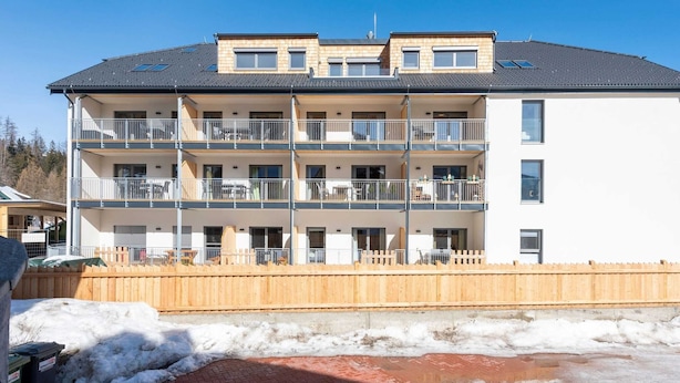 Un edificio residencial de varios pisos con balcones, planta baja de ladrillo y cerramiento de madera.