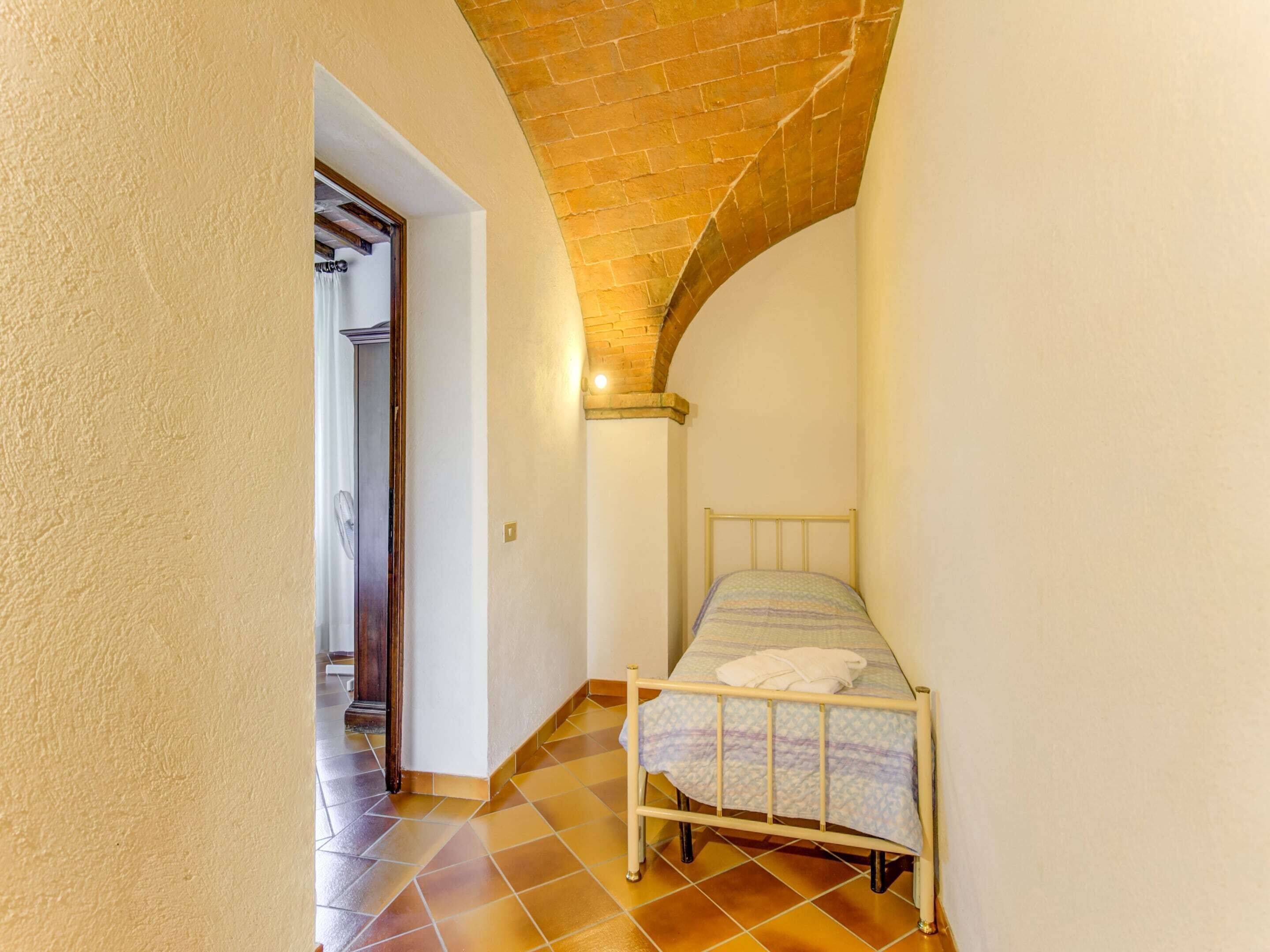 Une petite pièce avec un lit, un sol carrelé et un plafond en briques.