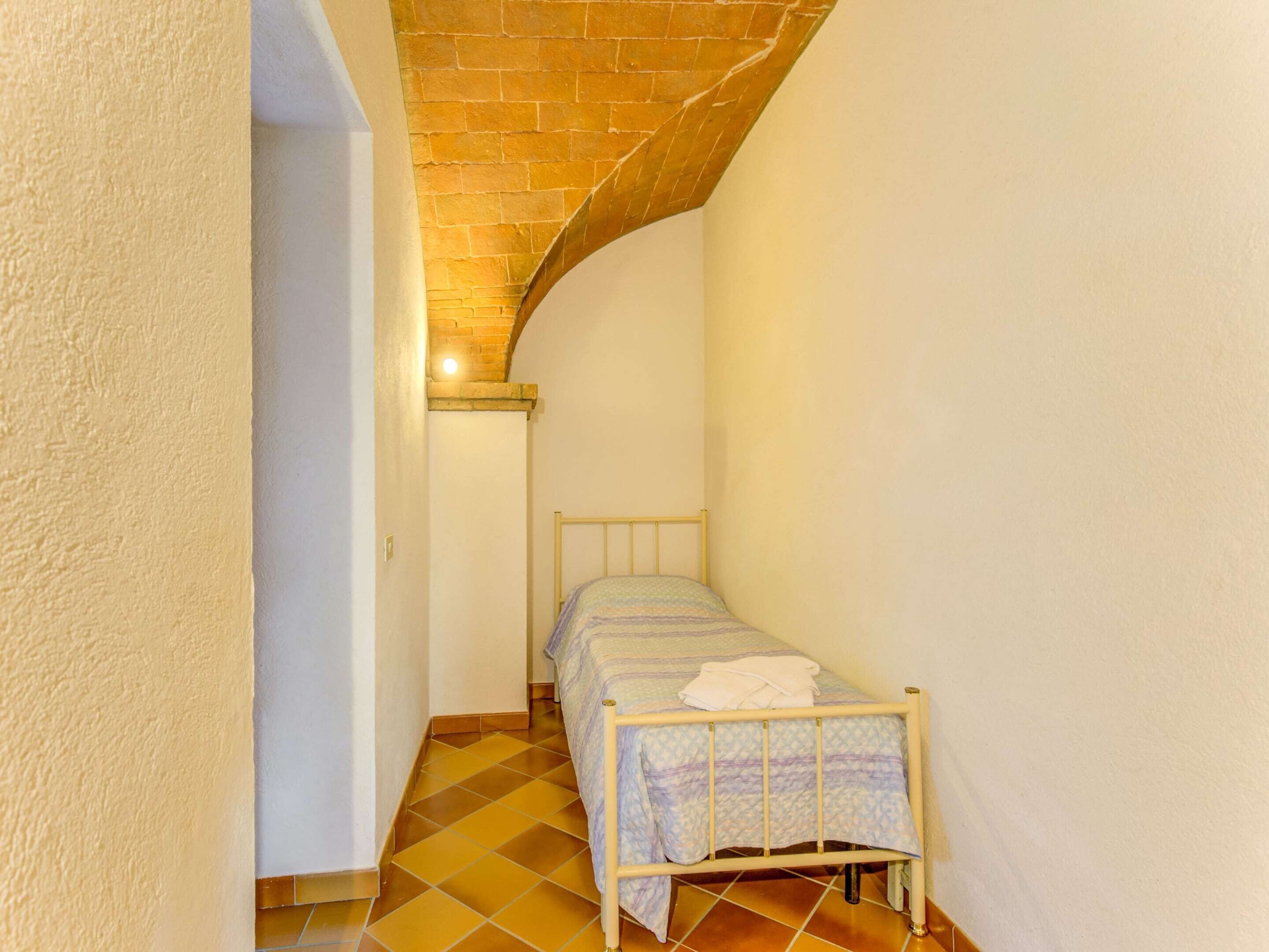 A narrow room with a bed, a tiled floor, and a brick ceiling.
