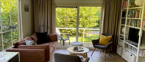 A spacious living room with a brown sofa, a grey armchair, a small round table, and a bookshelf filled with books.