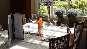 A table set for dining with a menu, wine bottle, and potted plants. - Comfy Chalet with Palletstove near Wadden Sea (Hippolytushoef)